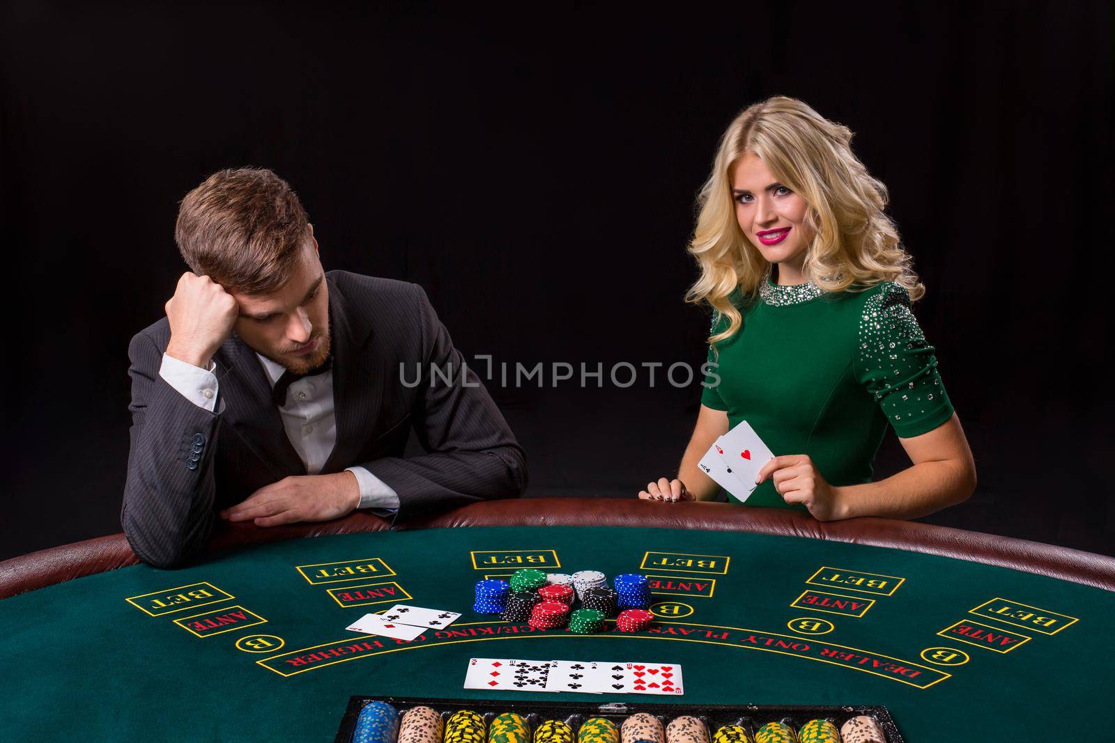 couple playing poker at the green table. The blonde girl and a guy in a suit. happy win, two aces