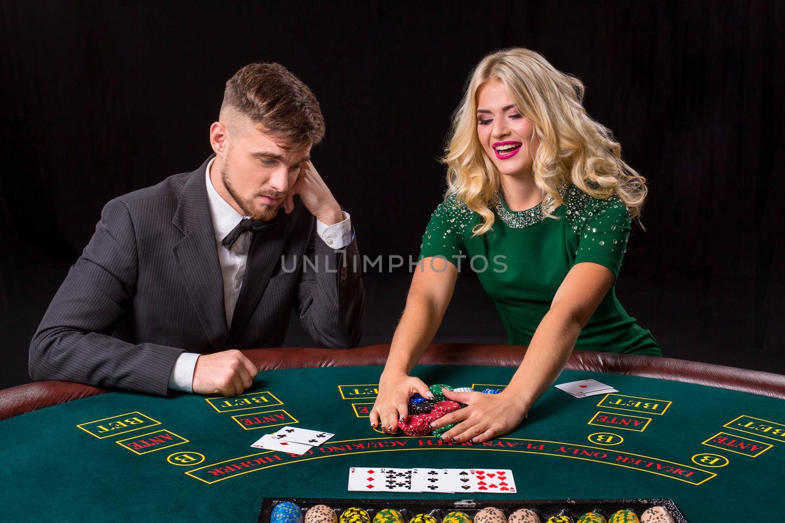 couple playing poker at the green table. The blonde girl and a guy in a suit. happy win