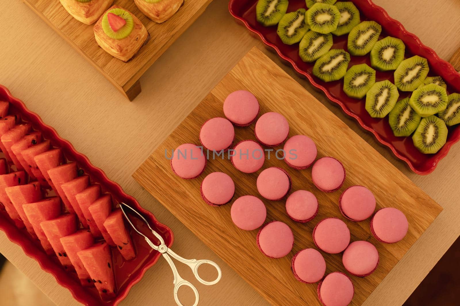 From above appetizing pink macaroons fresh watermelon and sliced kiwi fruit served on cutting boards and red dishes