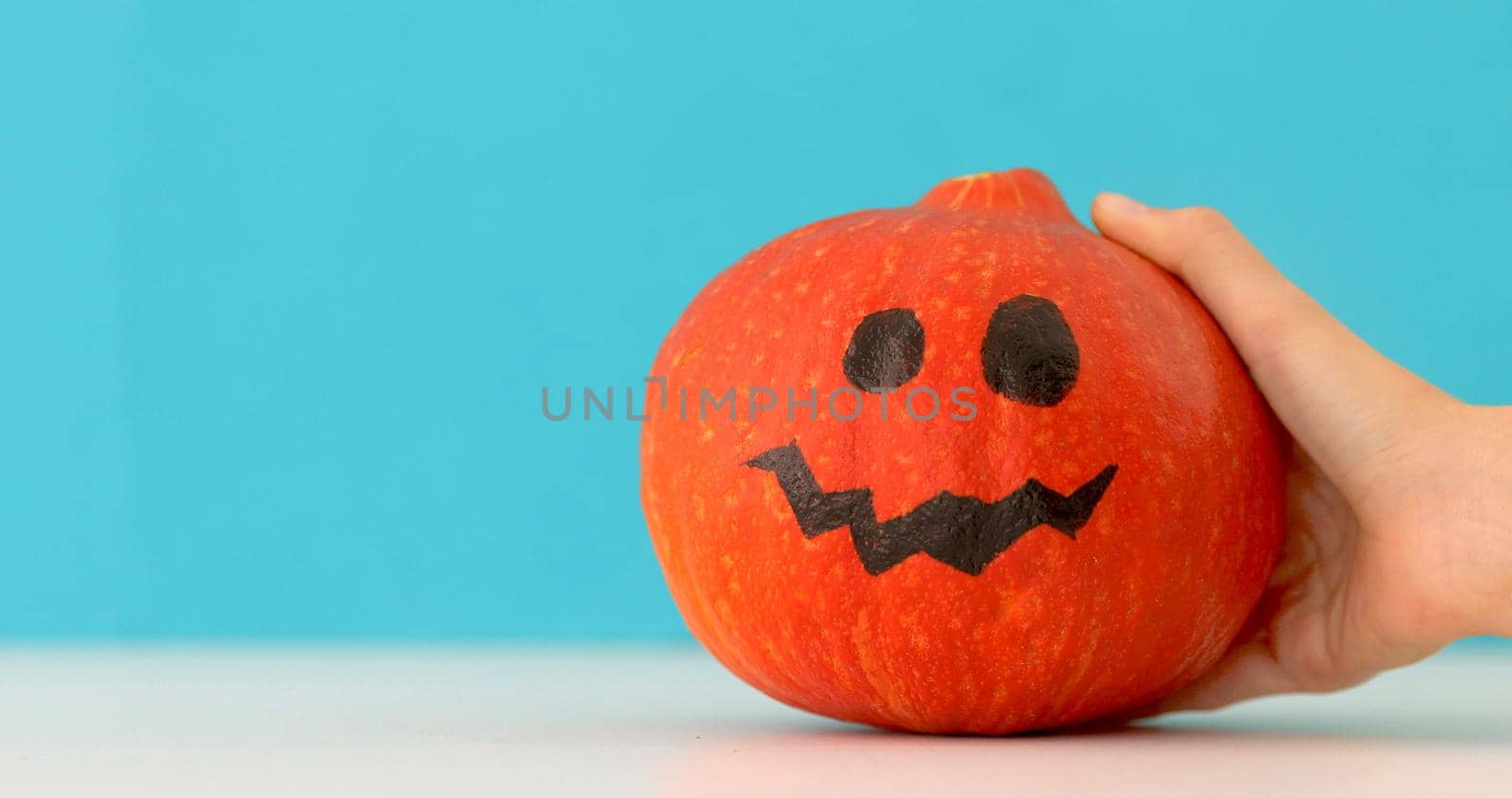 Little orange pumpkin dancing on blue background. Halloween holiday hand moves jack pumpkin