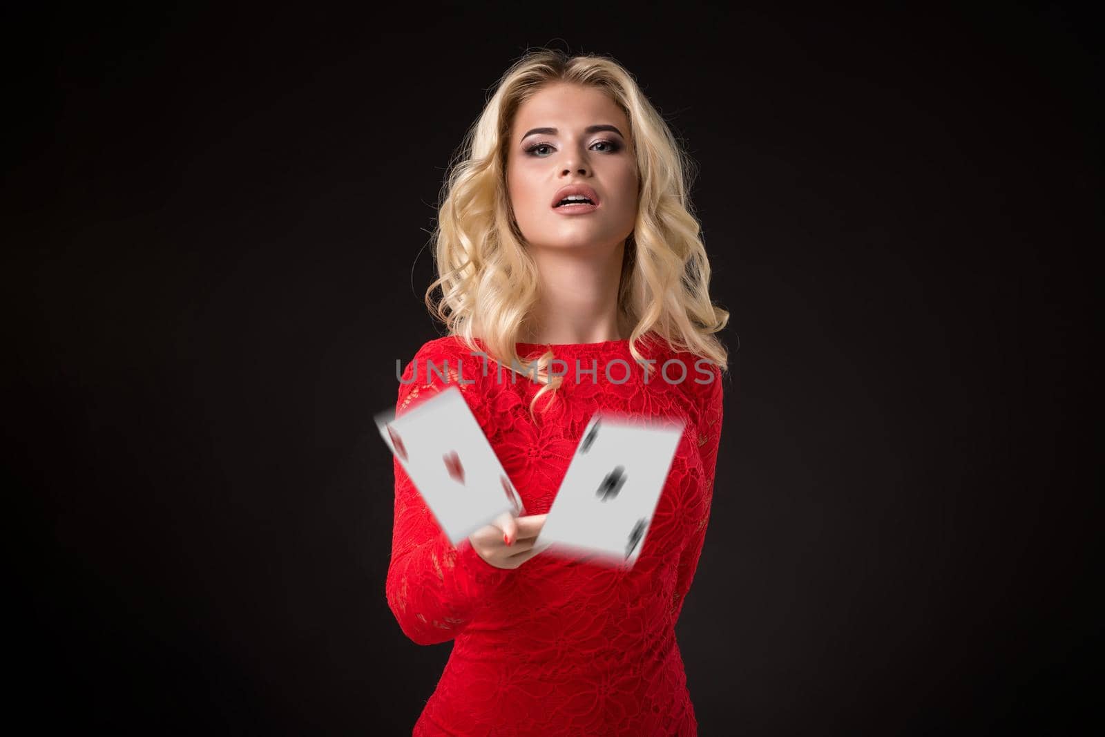 Young beautiful emotional woman throws cards on a black background in the studio. Poker by nazarovsergey