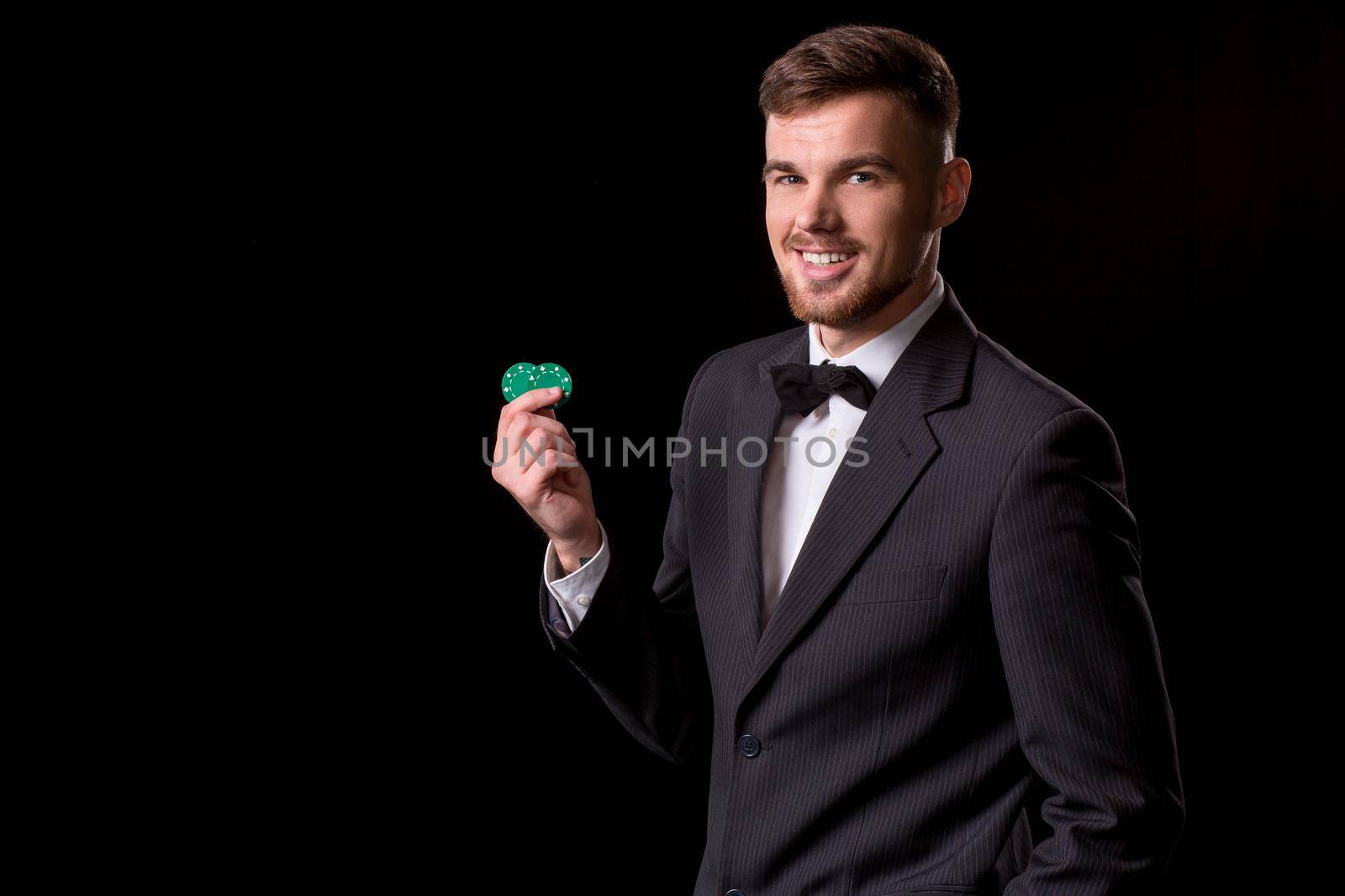 man in a suit posing with chips for gambling on black background