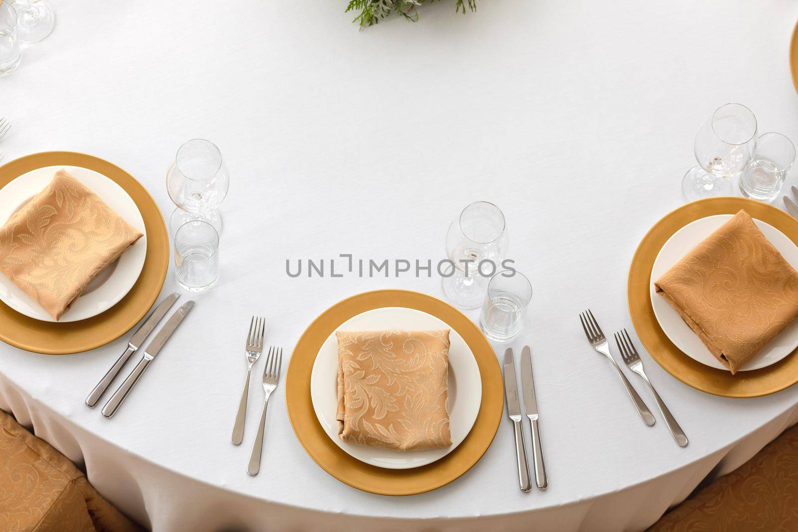 Top view of elegant plates with folded napkins and glassware served on clean white cloth in restaurant