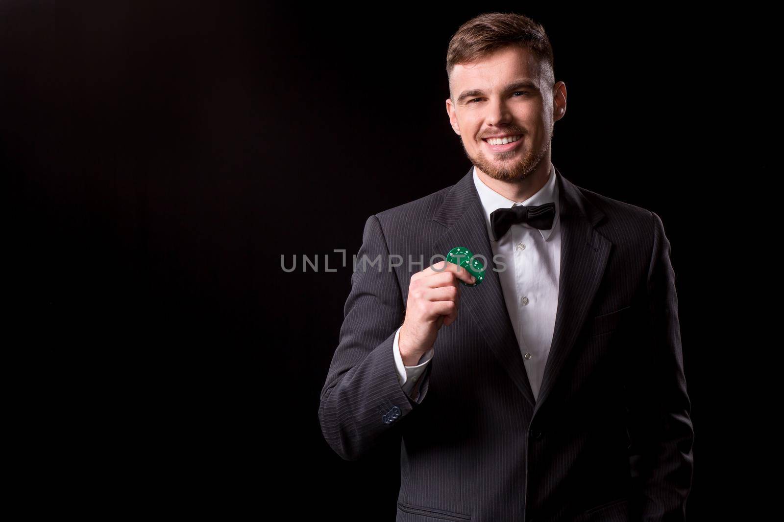 man in a suit posing with chips for gambling on black background