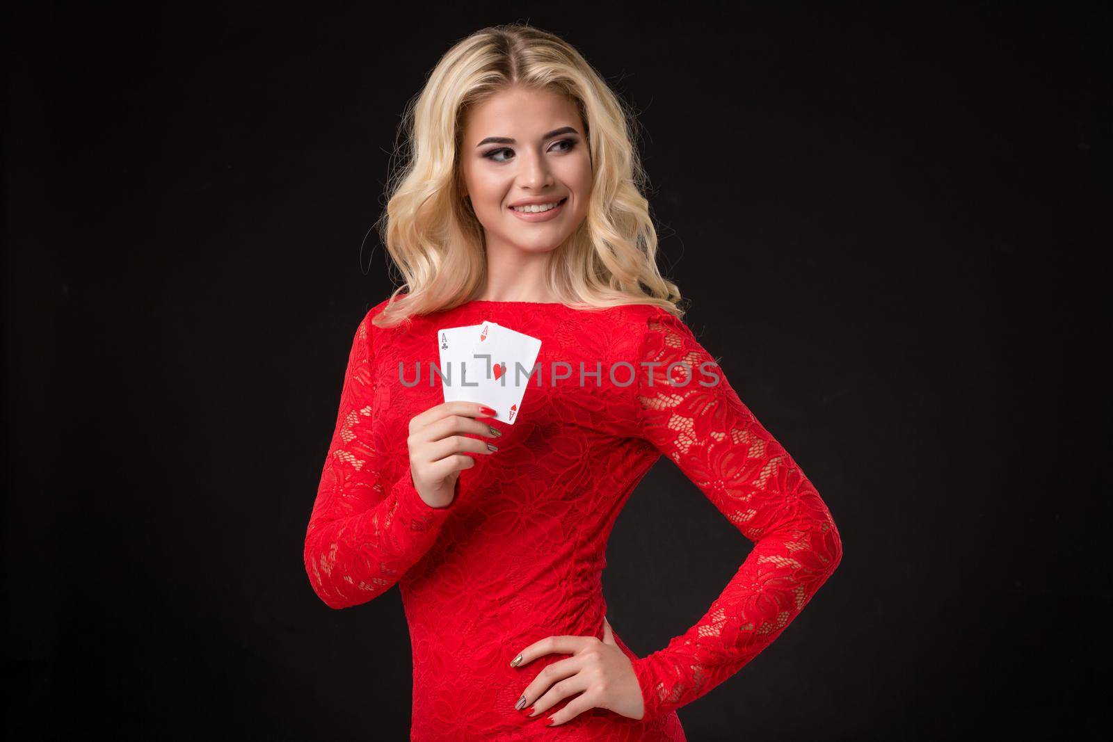 Young beautiful blond woman in a red dress with playing cards over black. Poker