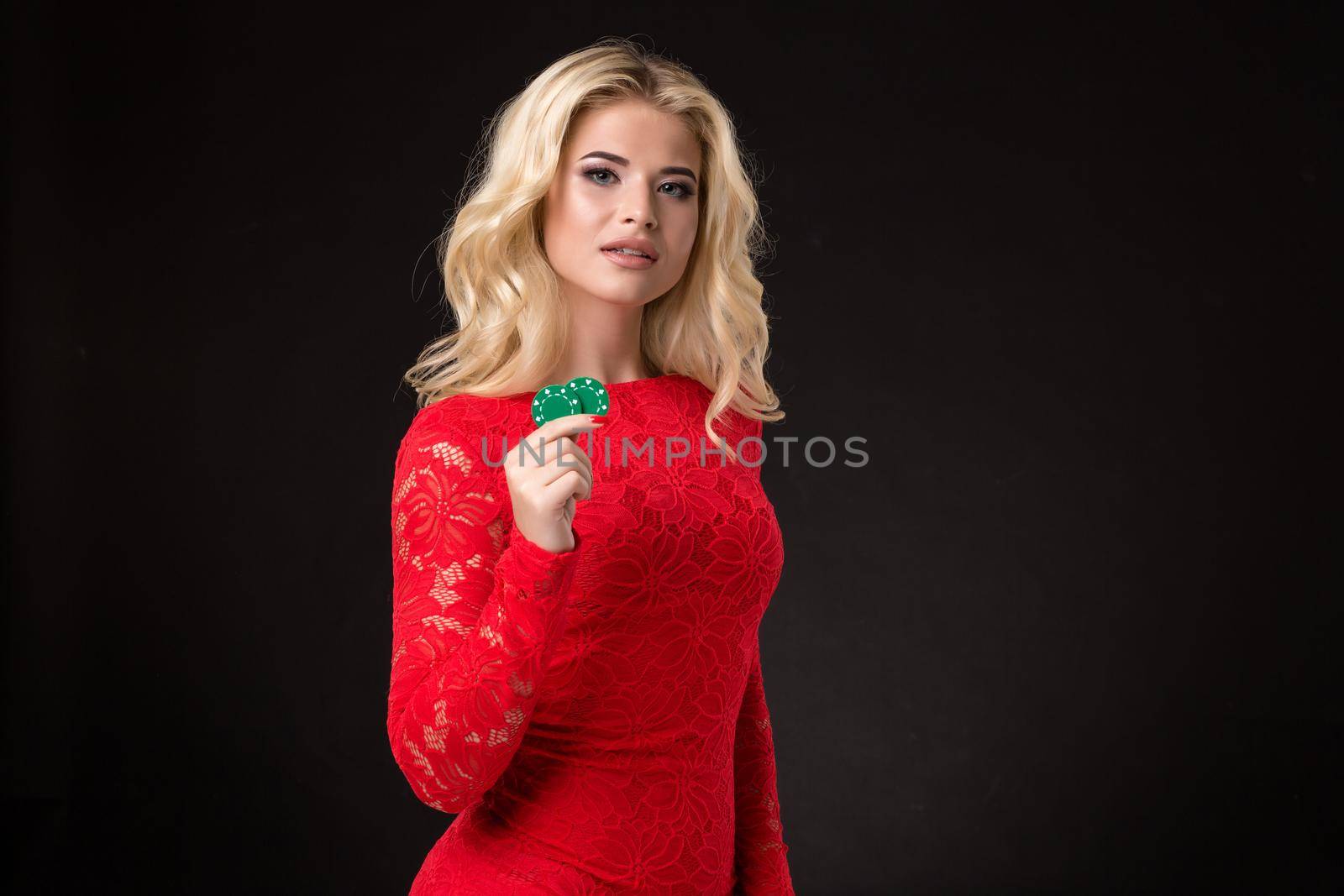Young beautiful blond woman in a red dress with poker chips over black. Poker