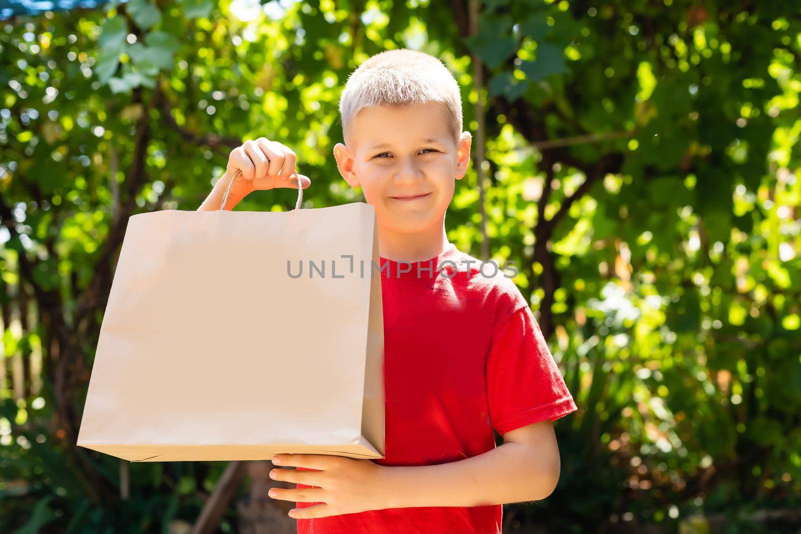 funny cute boy on green background. Holding bag of craft paper in his hands.