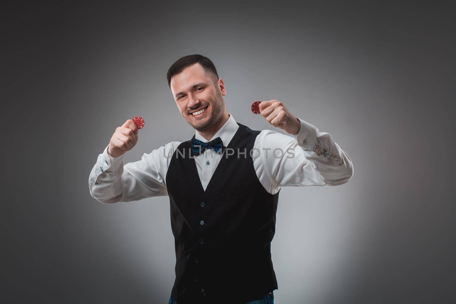 A man holding up red poker chips. Man in shirt and butterfly in studio on gray background. Poker