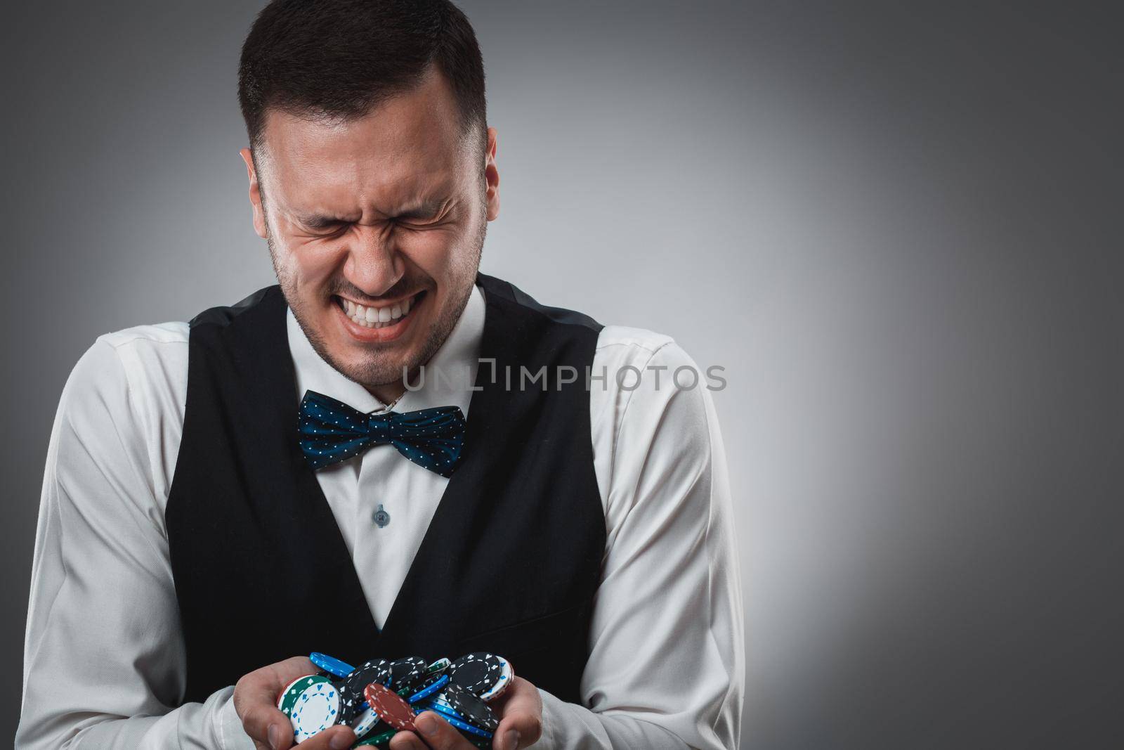 Young man in shirt and waistcoat shows his poker chips, studio shot. Poker. Emotions