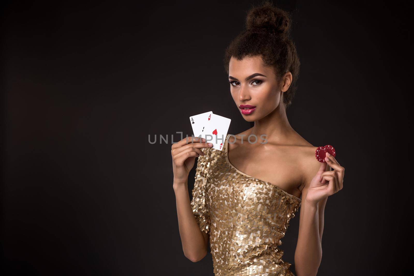 Woman winning - Young woman in a classy gold dress holding two aces and two red chips, a poker of aces card combination. Studio shot on black background