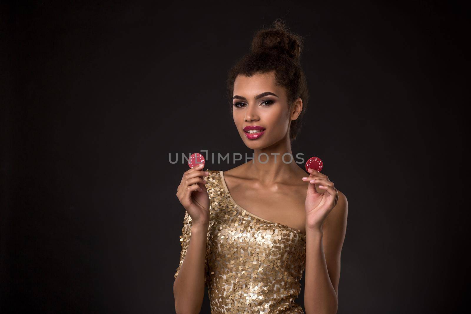 Woman winning - Young woman in a classy gold dress holding two red chips, a poker of aces card combination. Studio shot on black background