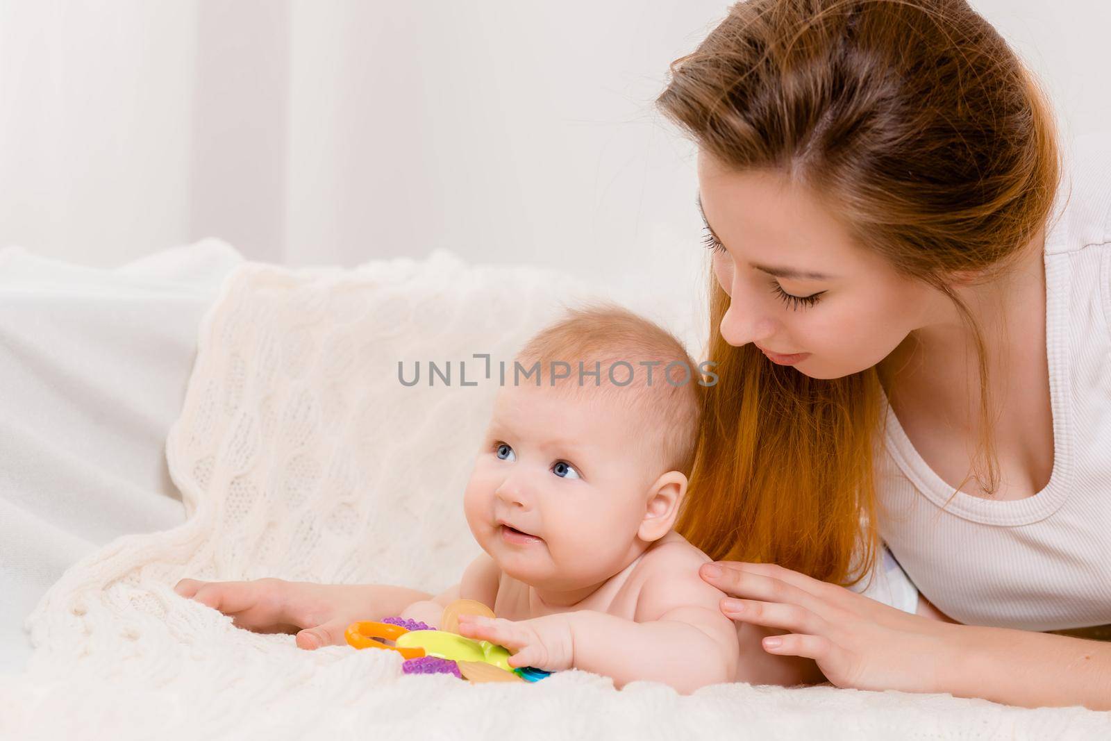 Mother and child on a white bed. Mom and baby boy in diaper playing in sunny bedroom. by nazarovsergey