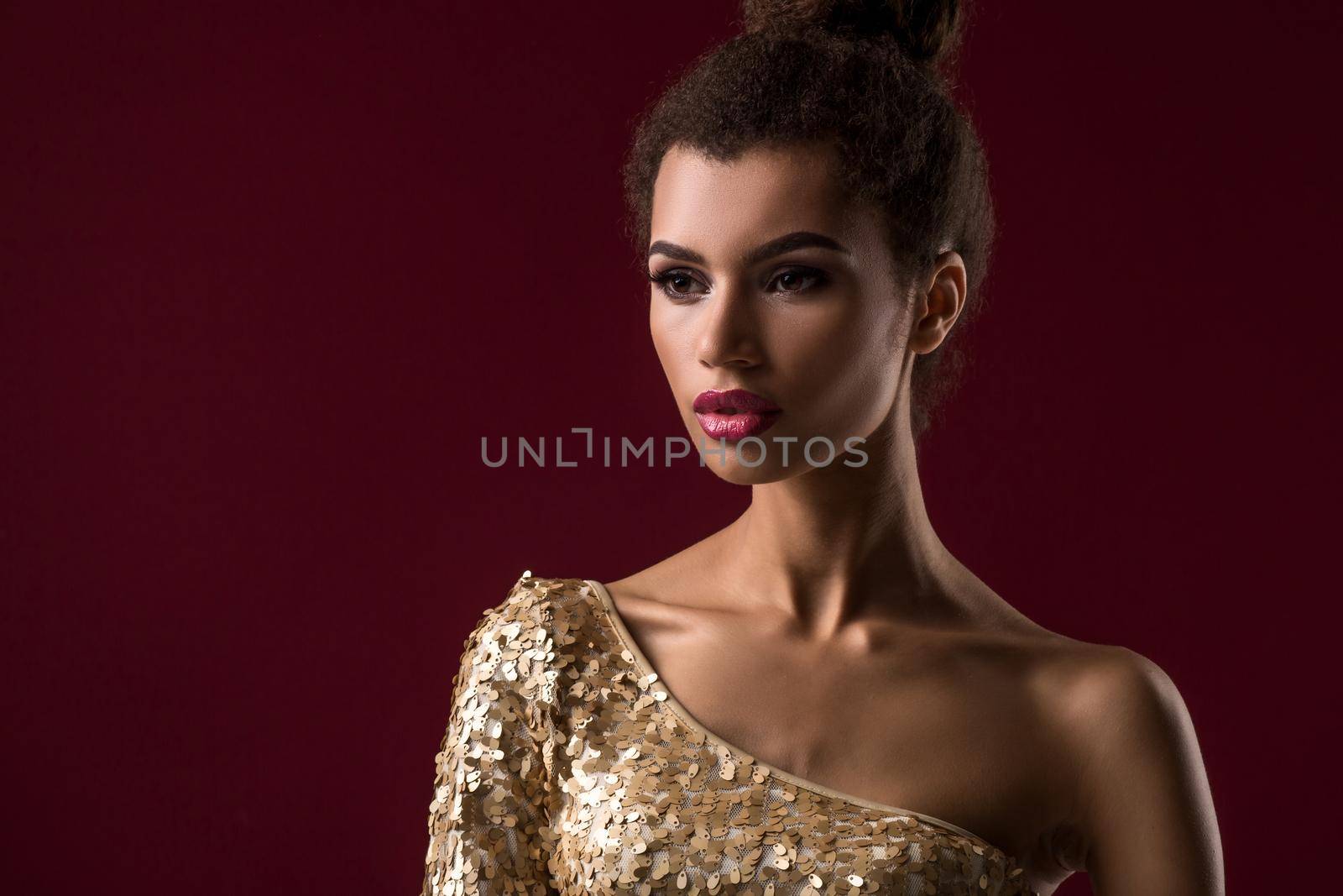Fashion young African woman with make-up, in sexy gold dress. Model on a claret background in the studio