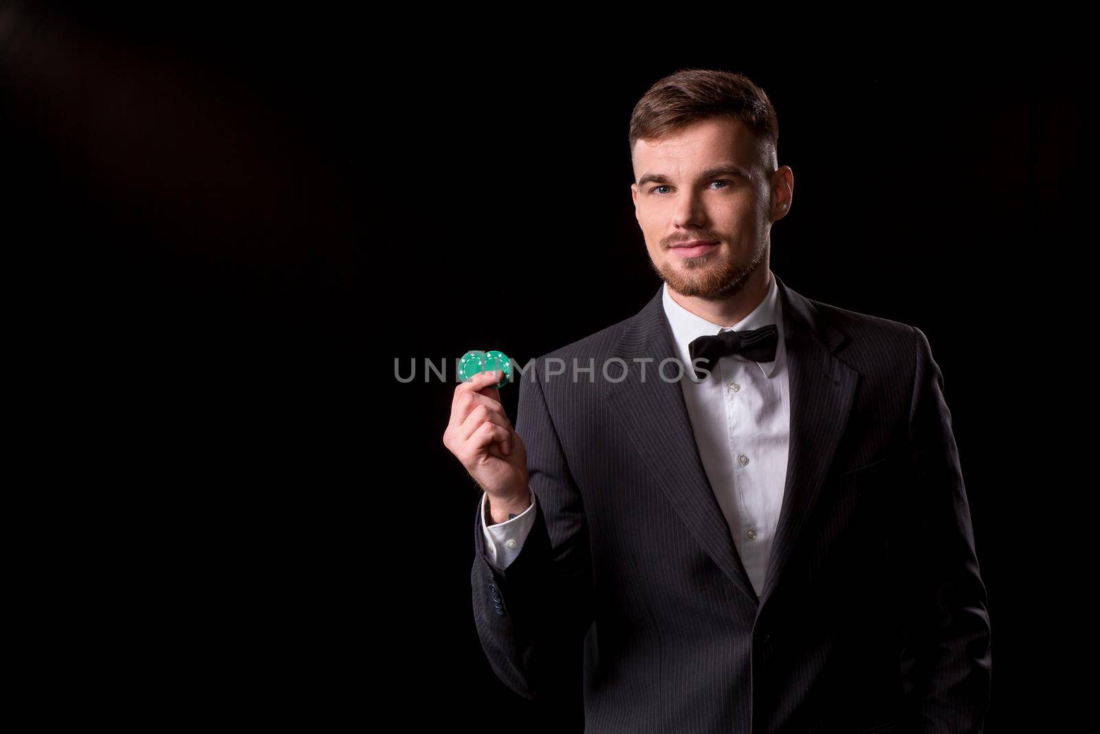 man in a suit posing with chips for gambling on black background