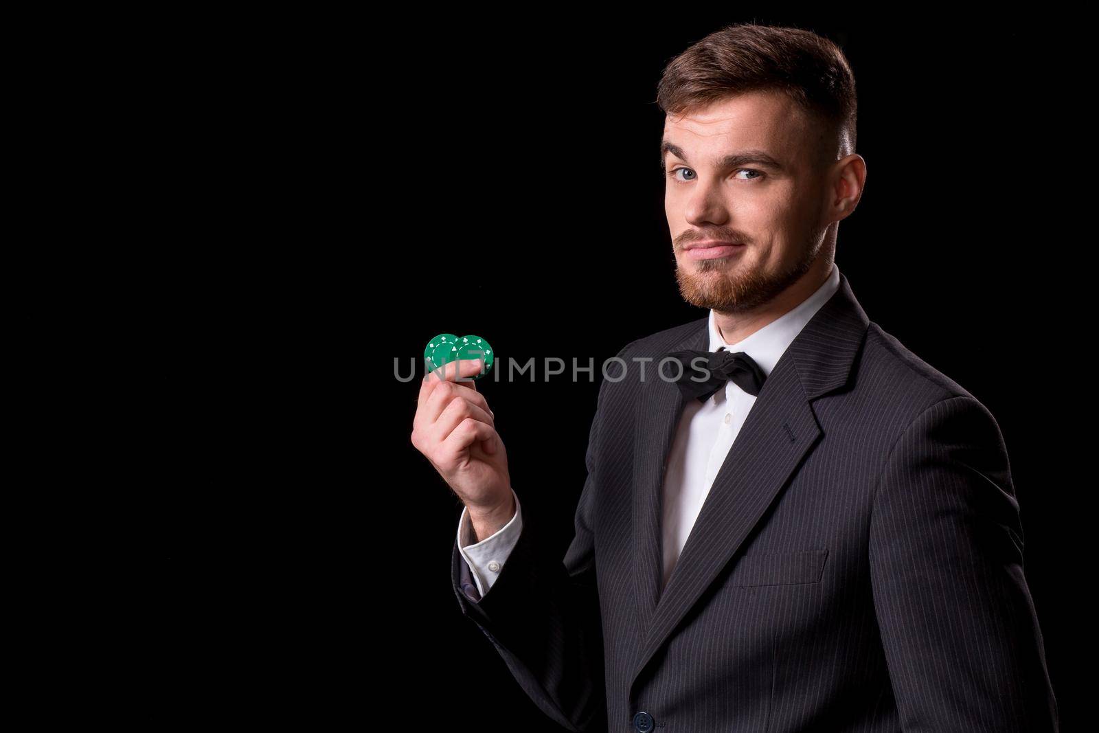 man in a suit posing with chips for gambling on black background