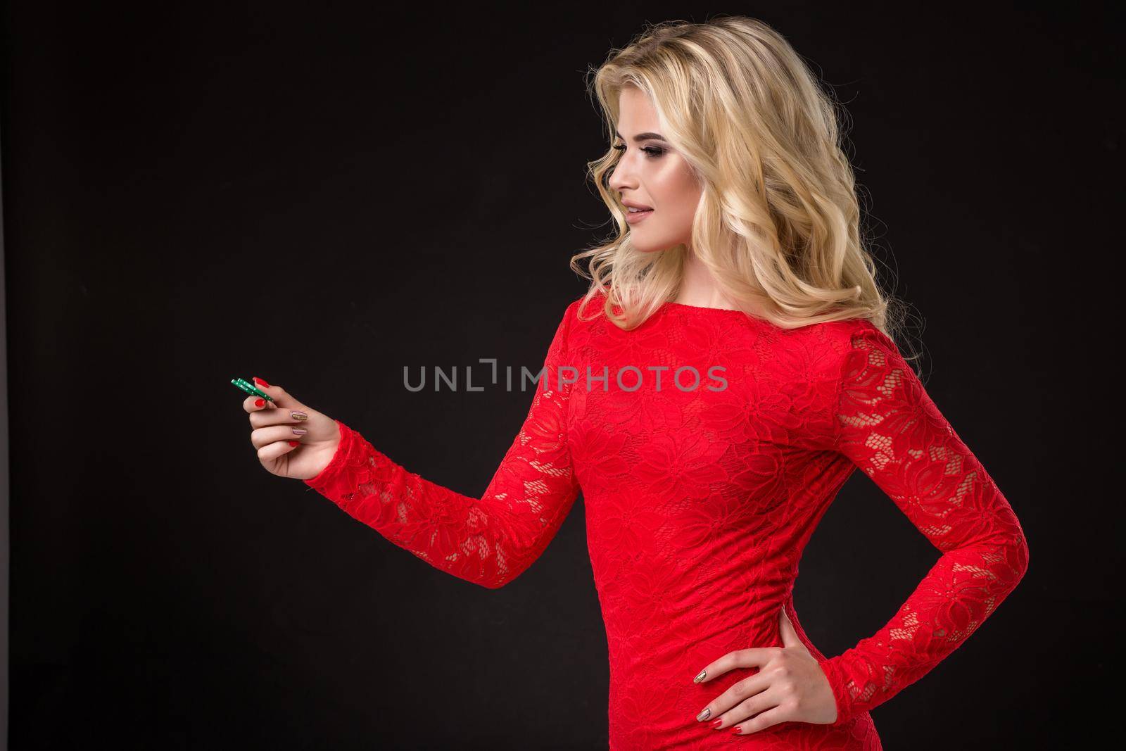 Young beautiful blond woman in a red dress with poker chips over black. Poker