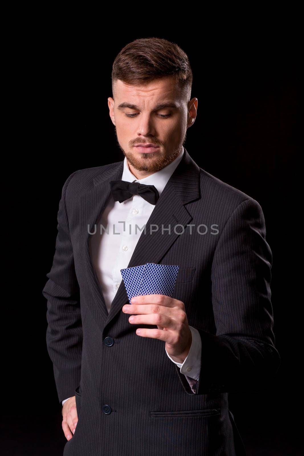 man in a suit posing with cards for gambling on black background