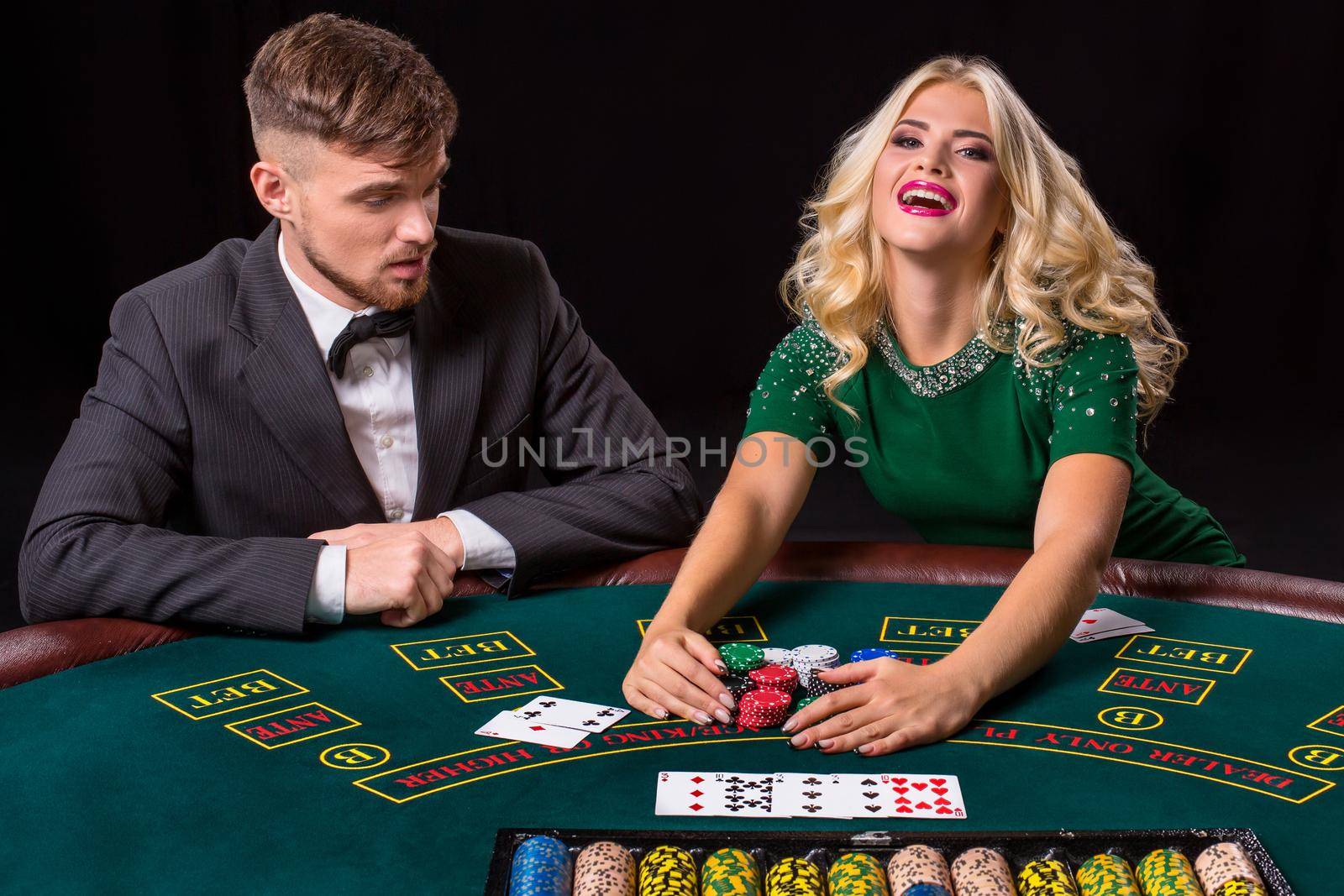 couple playing poker at the green table. The blonde girl and a guy in a suit. happy win