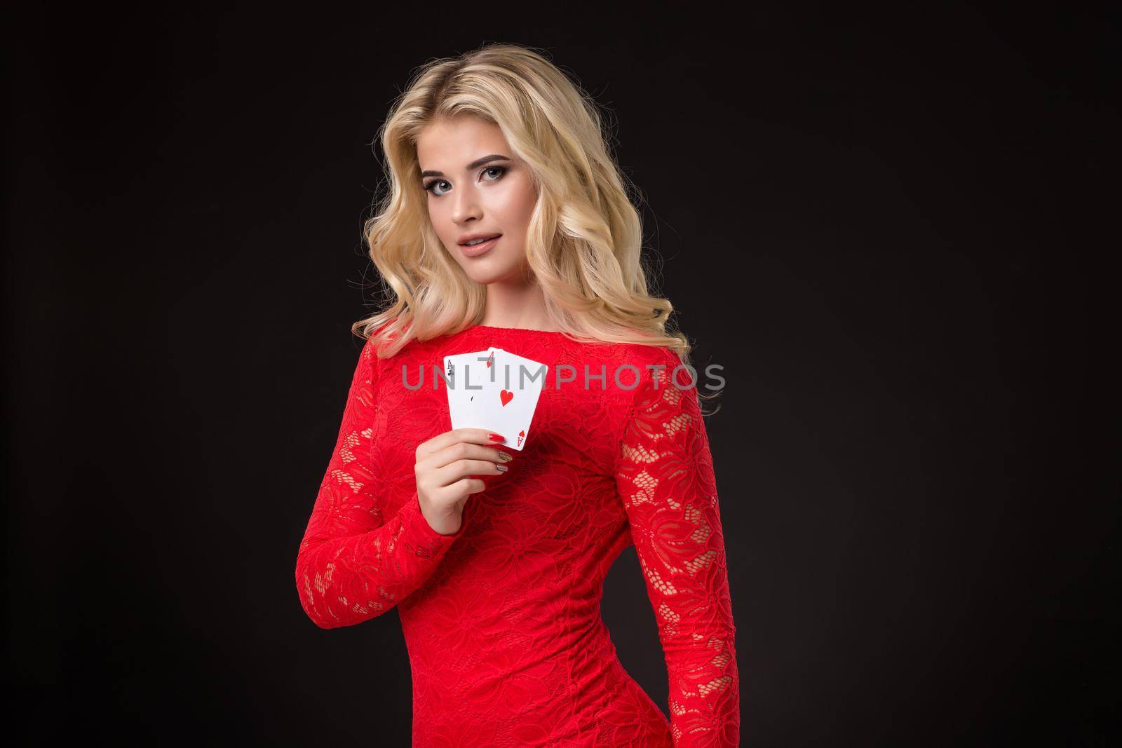Young beautiful blond woman in a red dress with playing cards over black. Poker
