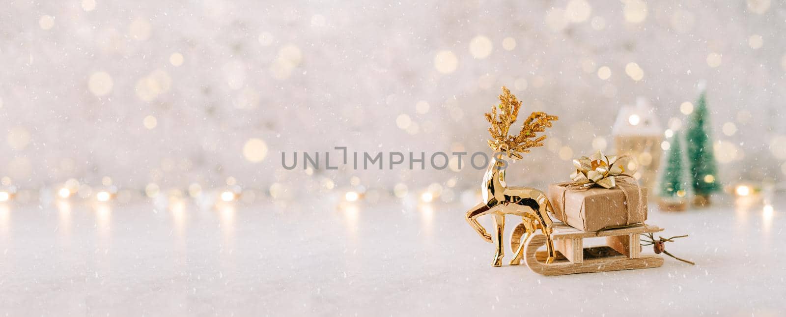 Golden deer dragging Natural Christmas gift on toy wooden sled on white background with glowing light bokeh, copy space. New year card. Xmas decoration, Christmas tree. Banner for design