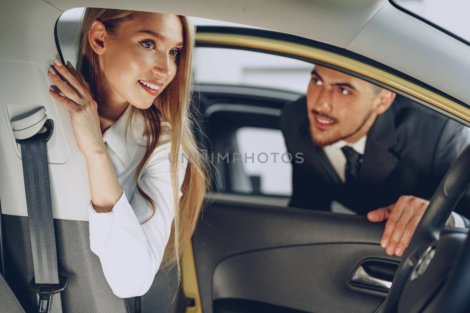 Man car dealer showing a woman buyer a new car in car salon