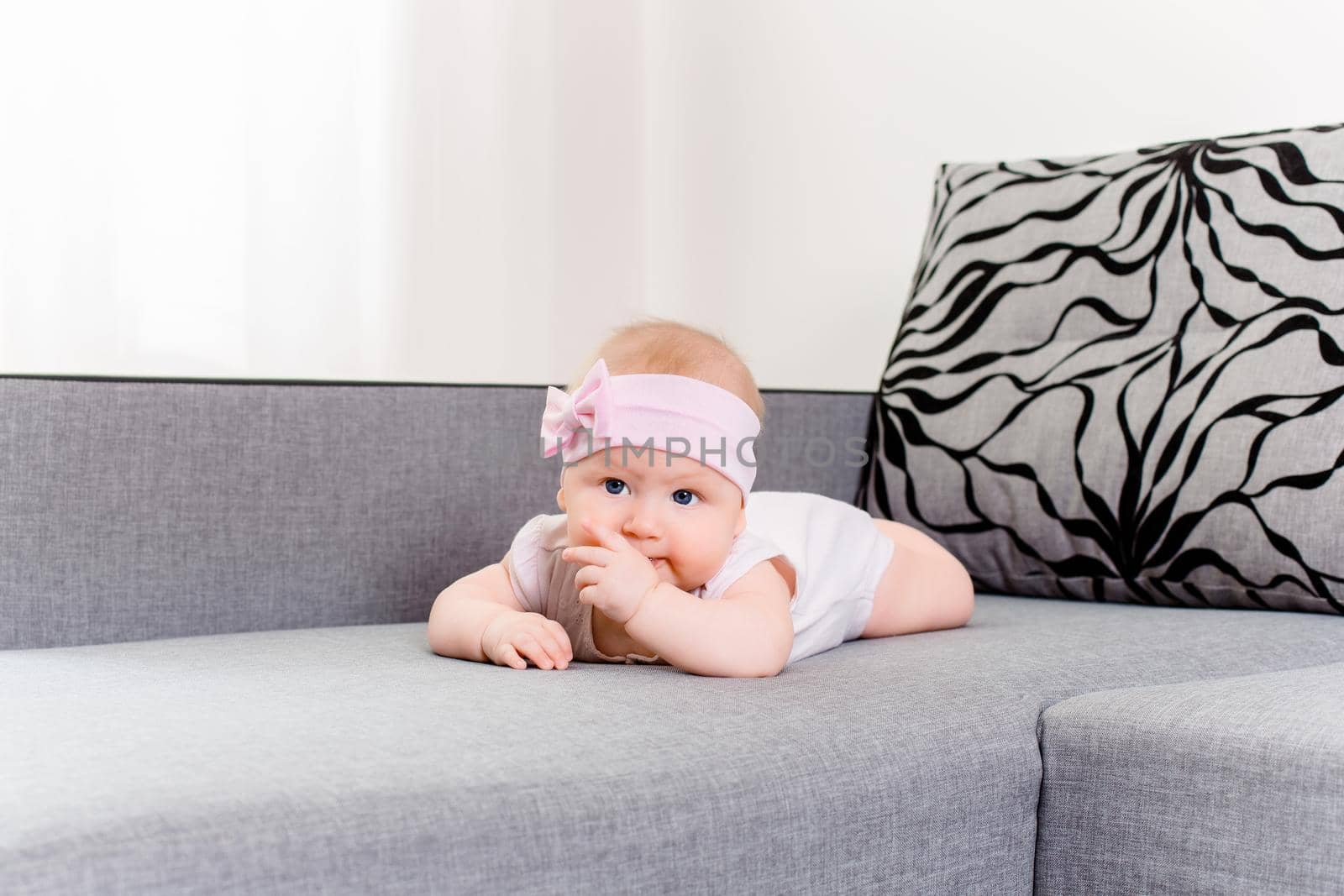 Portrait of a baby girl with a bandage and a bow on her head on a sofa by nazarovsergey