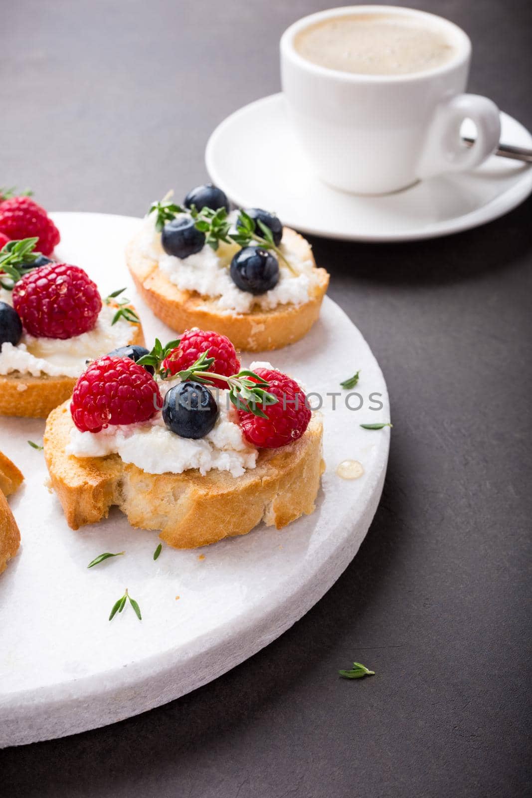 Cup of coffee with berry and goat cheese sandwiches on marble cutting board, top view, copy space.