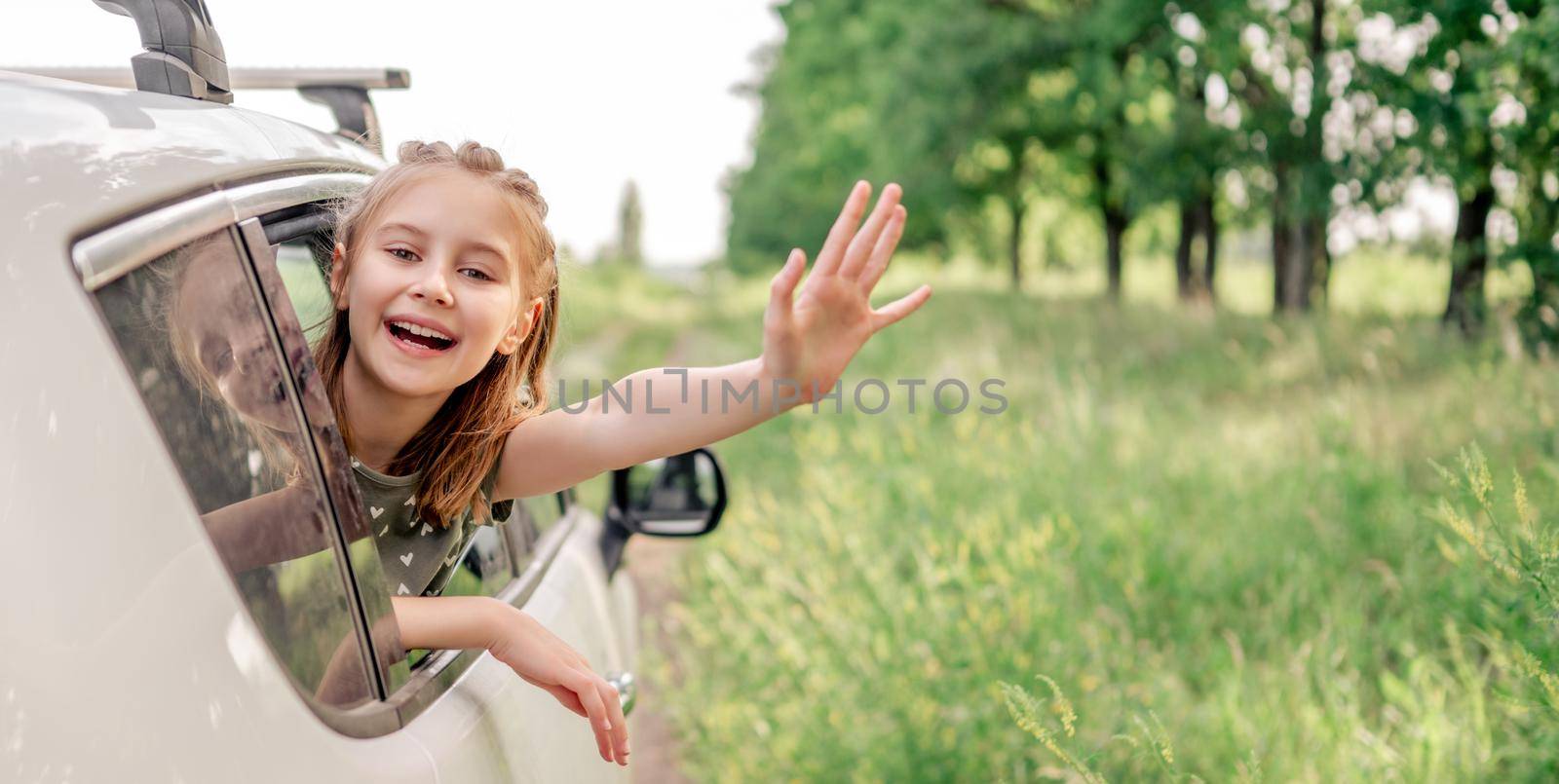 Beautiful preteen girl sitting in the car and looking out the window open and smiling. Happy child kid in the vehicle outdoors in the field during summer journey