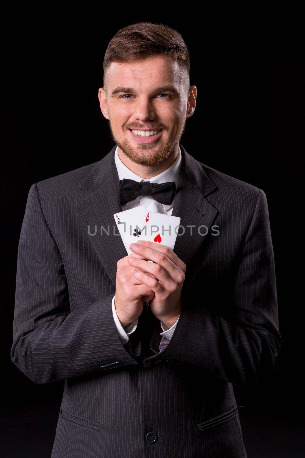 man in a suit posing with cards for gambling on black background