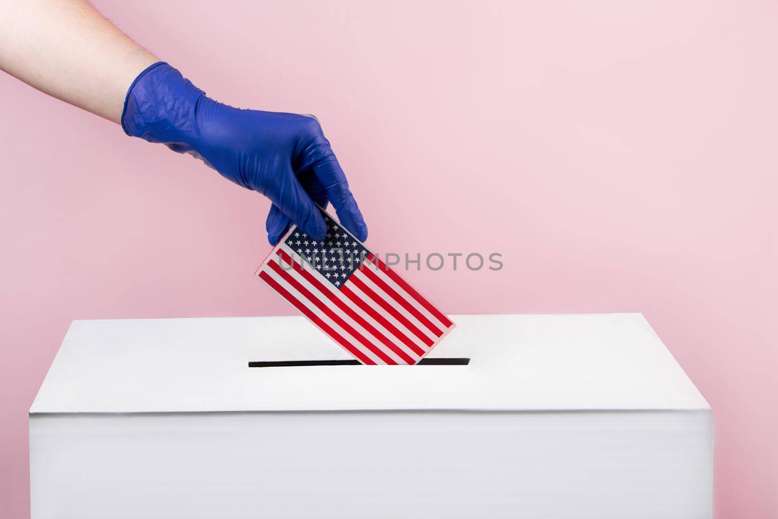 Woman in blue protective gloves puts the USA flag in a voting box. Elections and coronavirus concept.