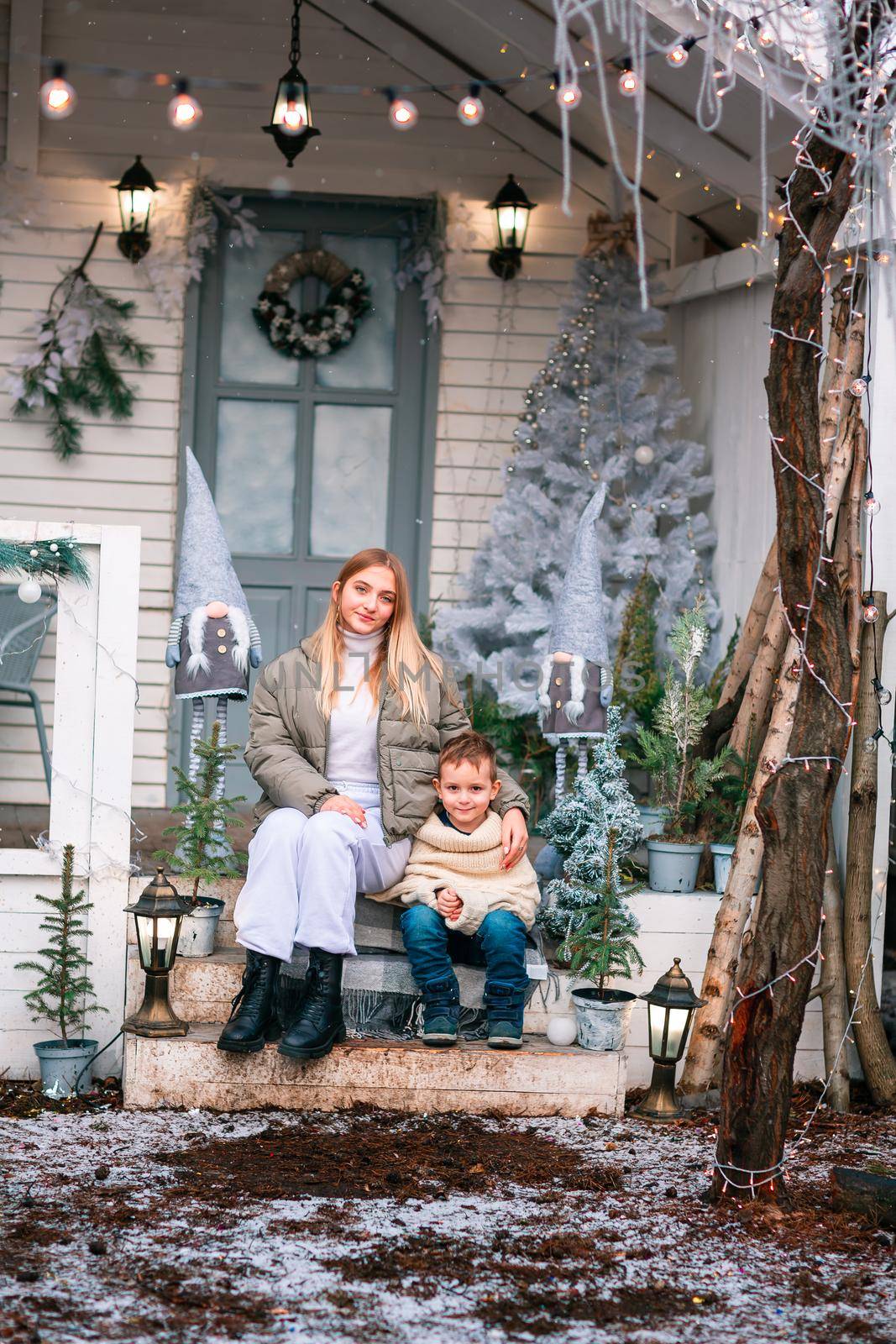 Happy little kids with white little puppy sitting on the porch of the Christmas decorated house, snowing outdoor. Happy New Year and Merry Christmas. Magic winter