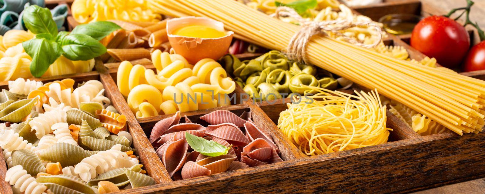 Spaghetti and assorted colorful italian pasta in wooden box. Healthy food background concept. Flat lay, top view. Banner.