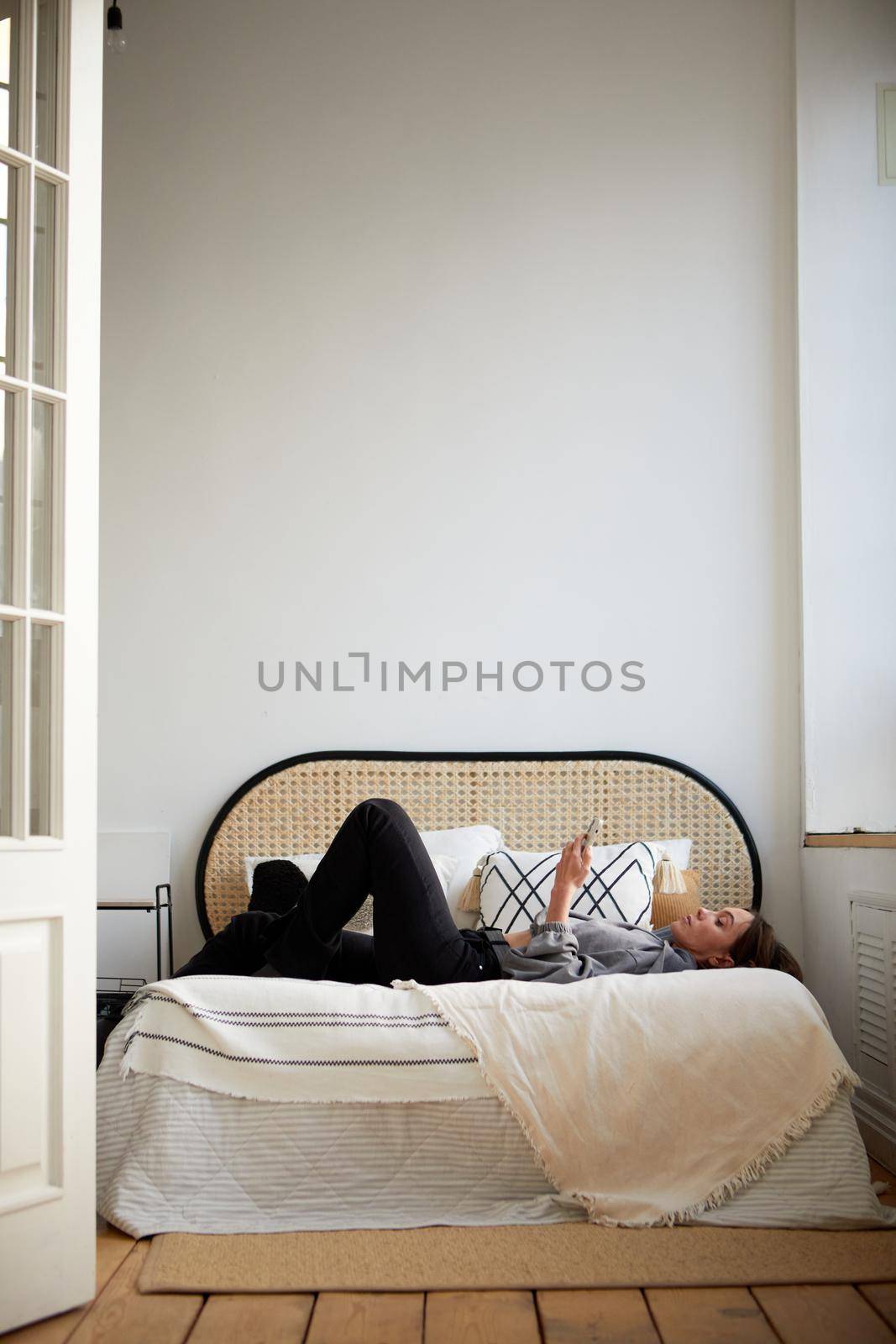 Woman lying on bed and browsing smartphone by Demkat