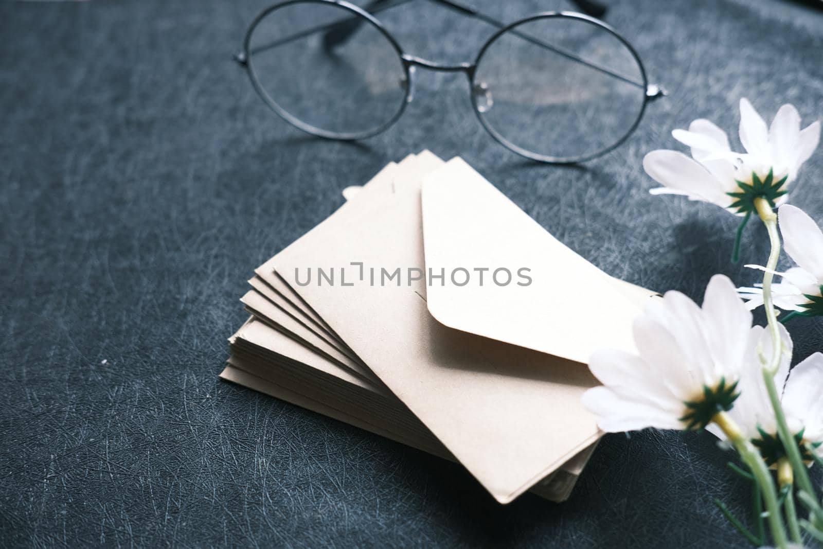 stack of envelope, eyeglass and flower on black background .