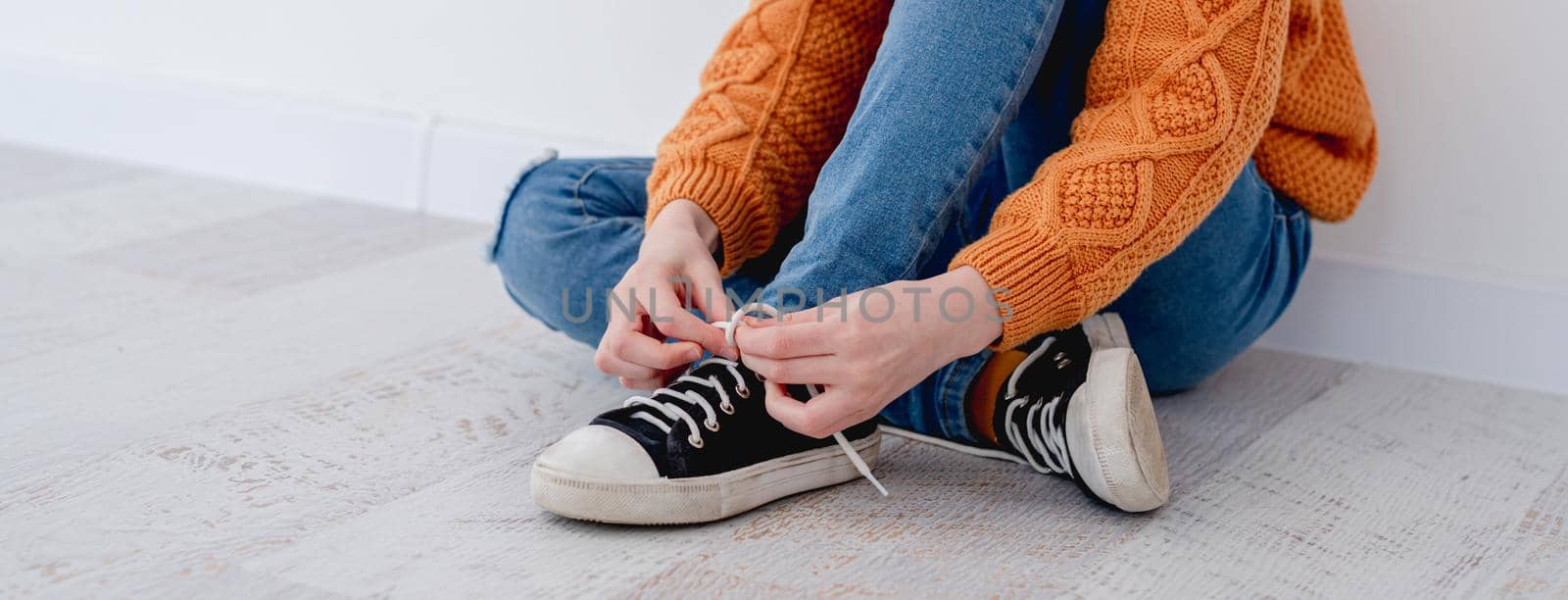 Little girl tying shoelace on sneakers while sitting on floor at home