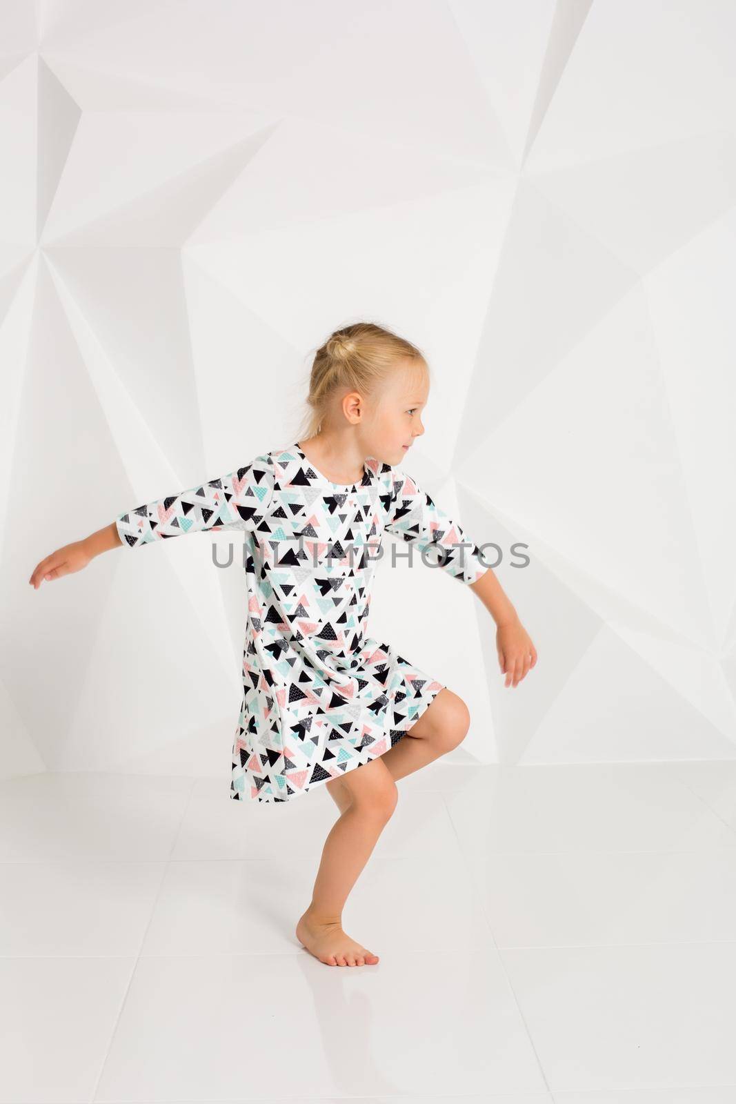 Beautiful little fashion model on white studio background. Portrait of cute girl posing in studio. Little blonde in bright summer dress