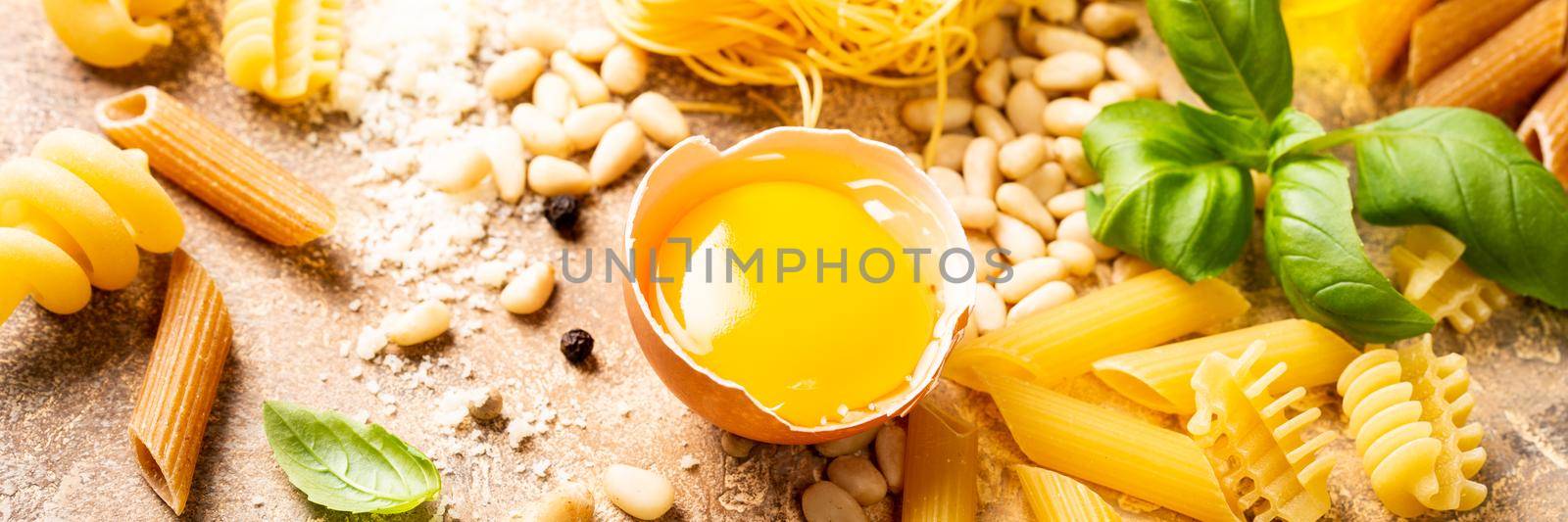 Healthy raw ingredients for italian pasta sauce Carbonara with egg, grated cheese, pine nuts, basil and assorted pasta. Food background. Banner.
