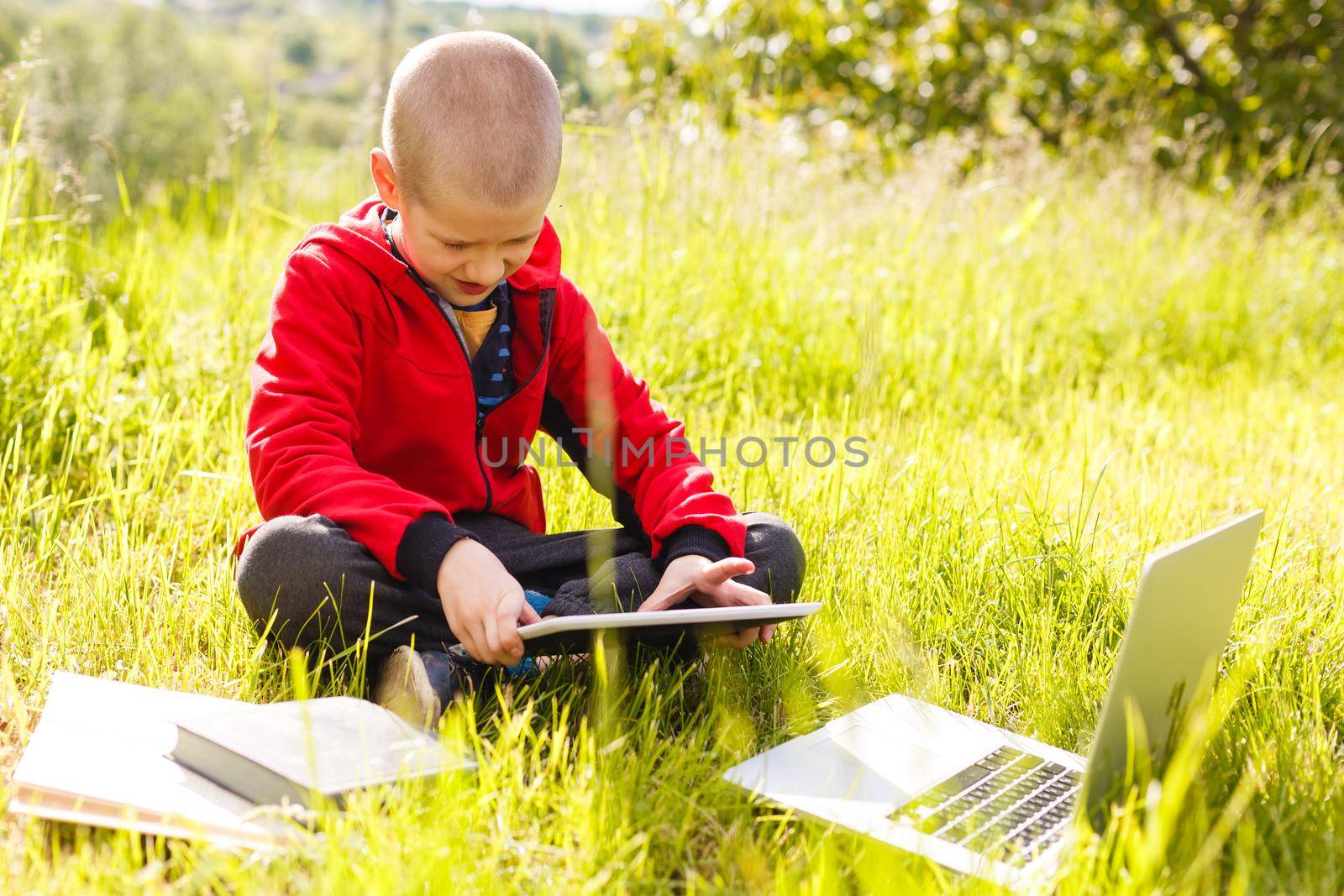 Distance learning. Boy learns autdoor laptop. Doing homework on grass. The child learns in the fresh air. The child's hands and computer by Andelov13