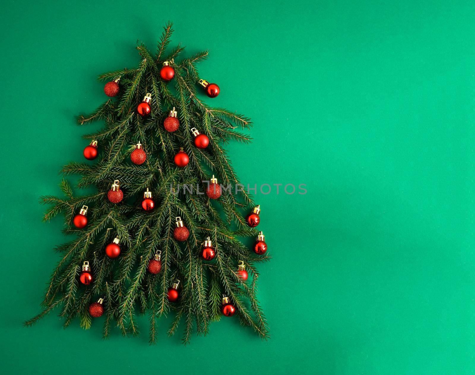 Christmas tree made of green coniferous branches on a green background. Christmas background with place for text. Christmas holiday concept. Ball toys. Red balls