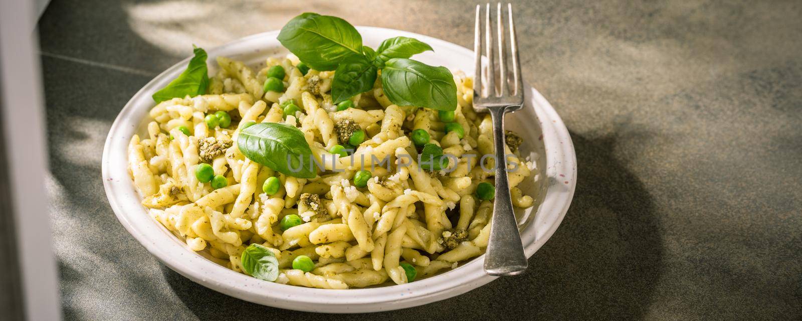 Homemade pasta Trofie from Liguria with green pesto, pea and basil. Italian healthy food concept with copy space. Banner.