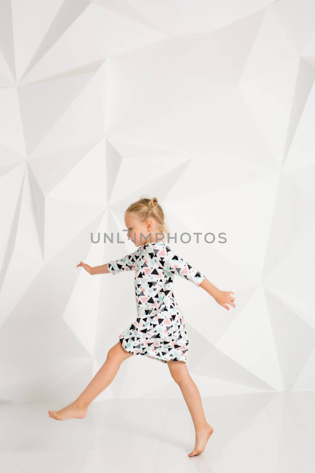 Beautiful little fashion model on white studio background. Portrait of cute girl posing in studio. Little blonde in bright summer dress