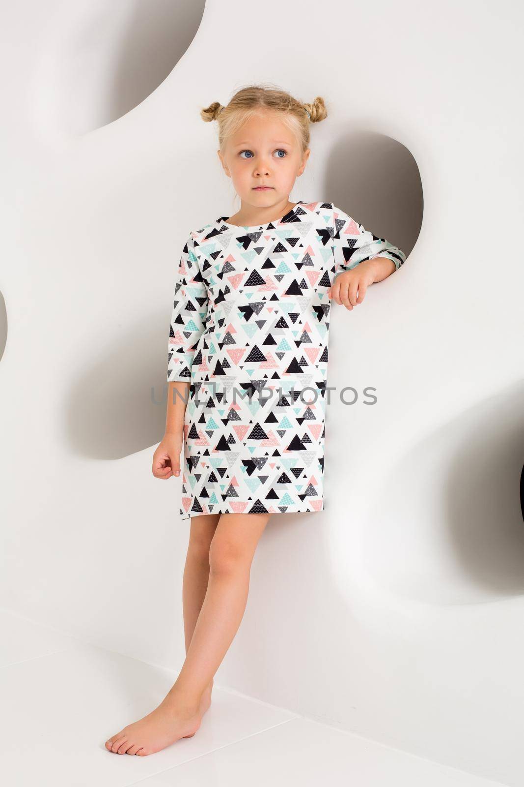 Beautiful little fashion model on white studio background. Portrait of cute girl posing in studio. Little blonde in bright summer dress