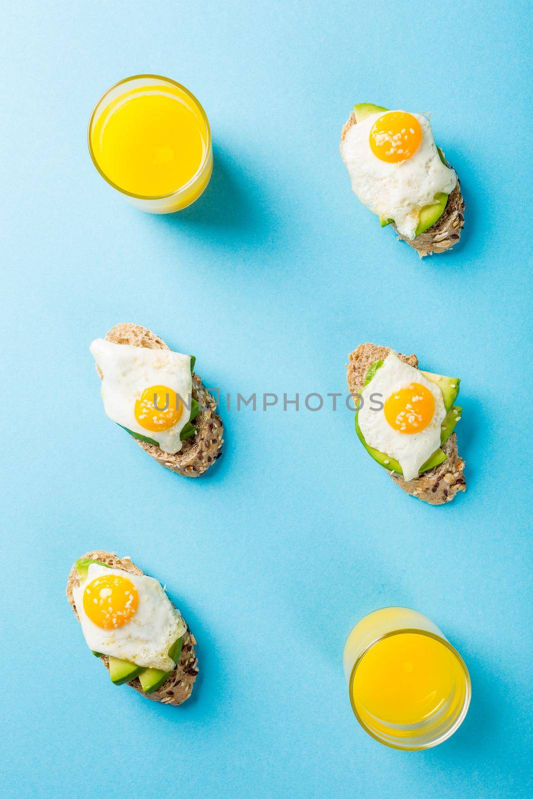 Flat lay with healthy sandwich with fresh avocado and fried quail egg on blue background. Breakfast or lunch food concept with copy space. Top view.