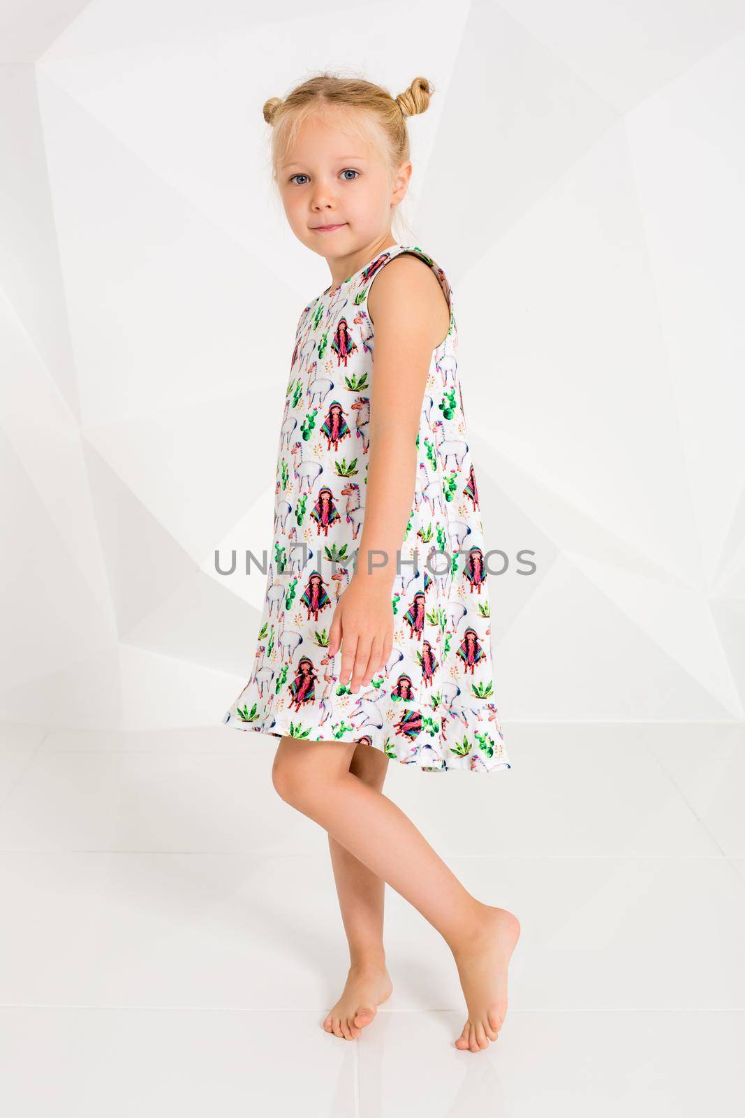 Beautiful little fashion model on white studio background. Portrait of cute girl posing in studio. Little blonde in bright summer dress