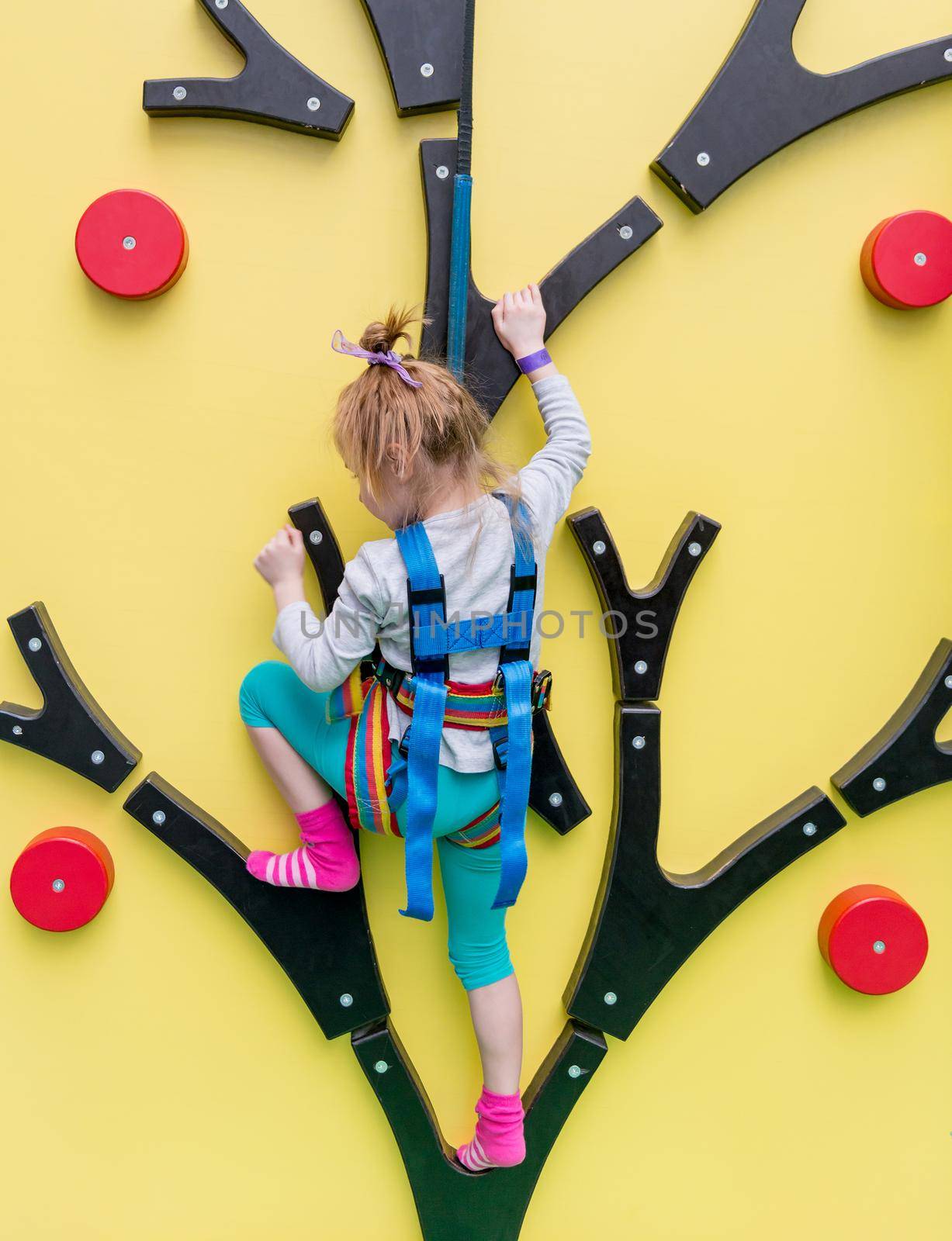 Little girl in insurance trains on climbing wall in indoor gym