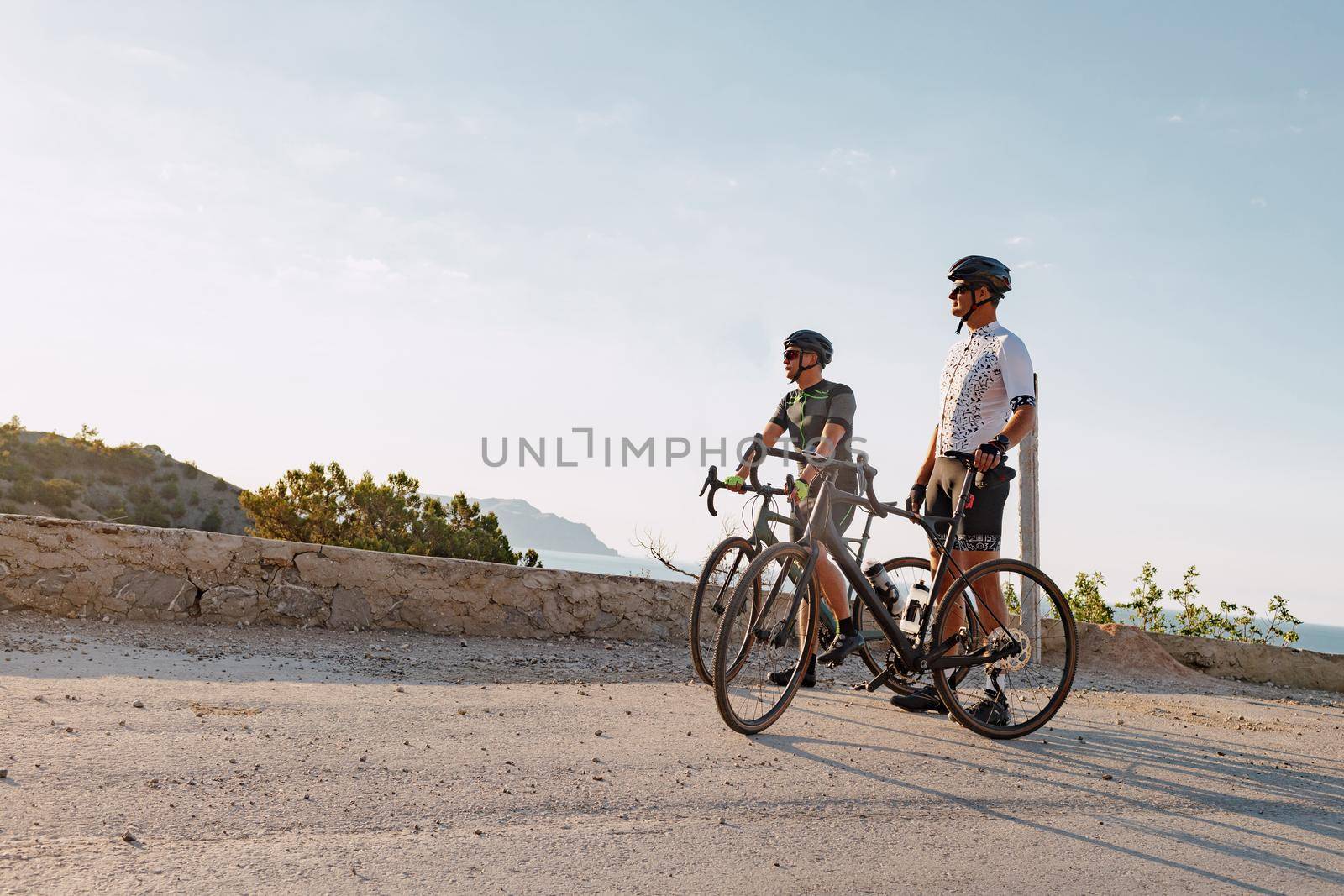 Two male cyclists stand on the coastal road and have a rest