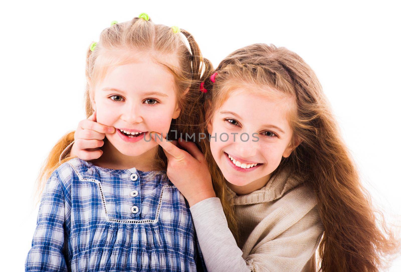 Girl put her fingers to the corners of the mouth to make her little sister smile. Two sisters having relaxing time together isolated on white background