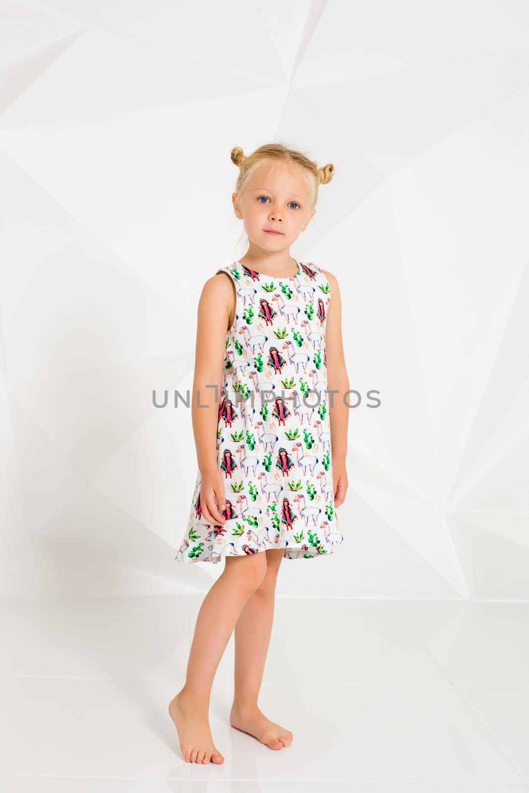 Beautiful little fashion model on white studio background. Portrait of cute girl posing in studio. Little blonde in bright summer dress