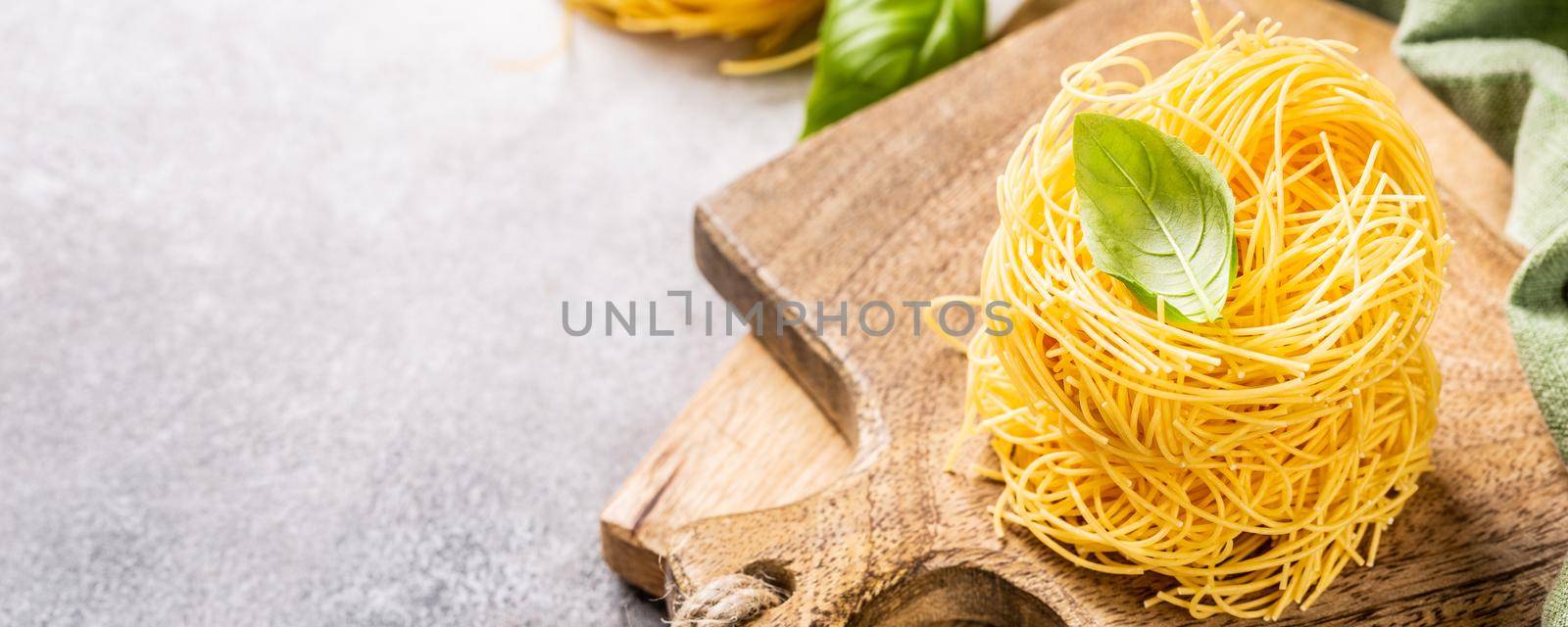 Fresh egg pasta tagliatelle nest on wooden cutting board with basil leaf. Healthy italian food concept with copy space. Banner.