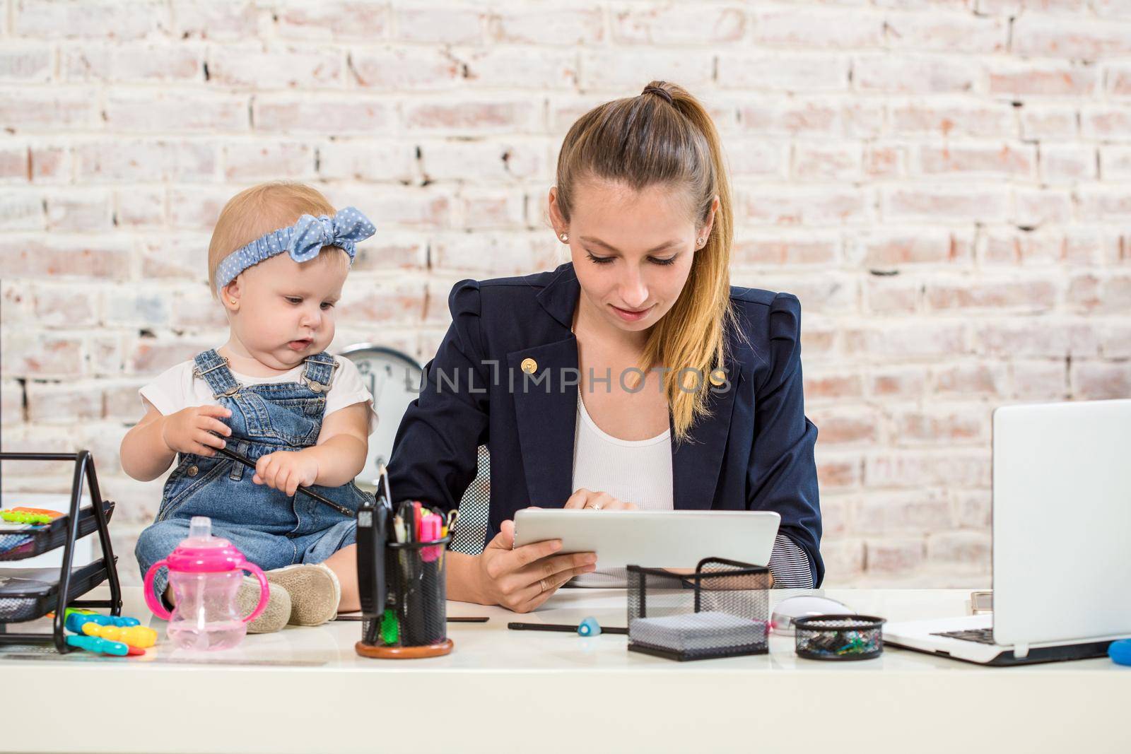 Mom and businesswoman working with laptop computer at home and playing with her baby girl. Horizontal shape, front view, waist up